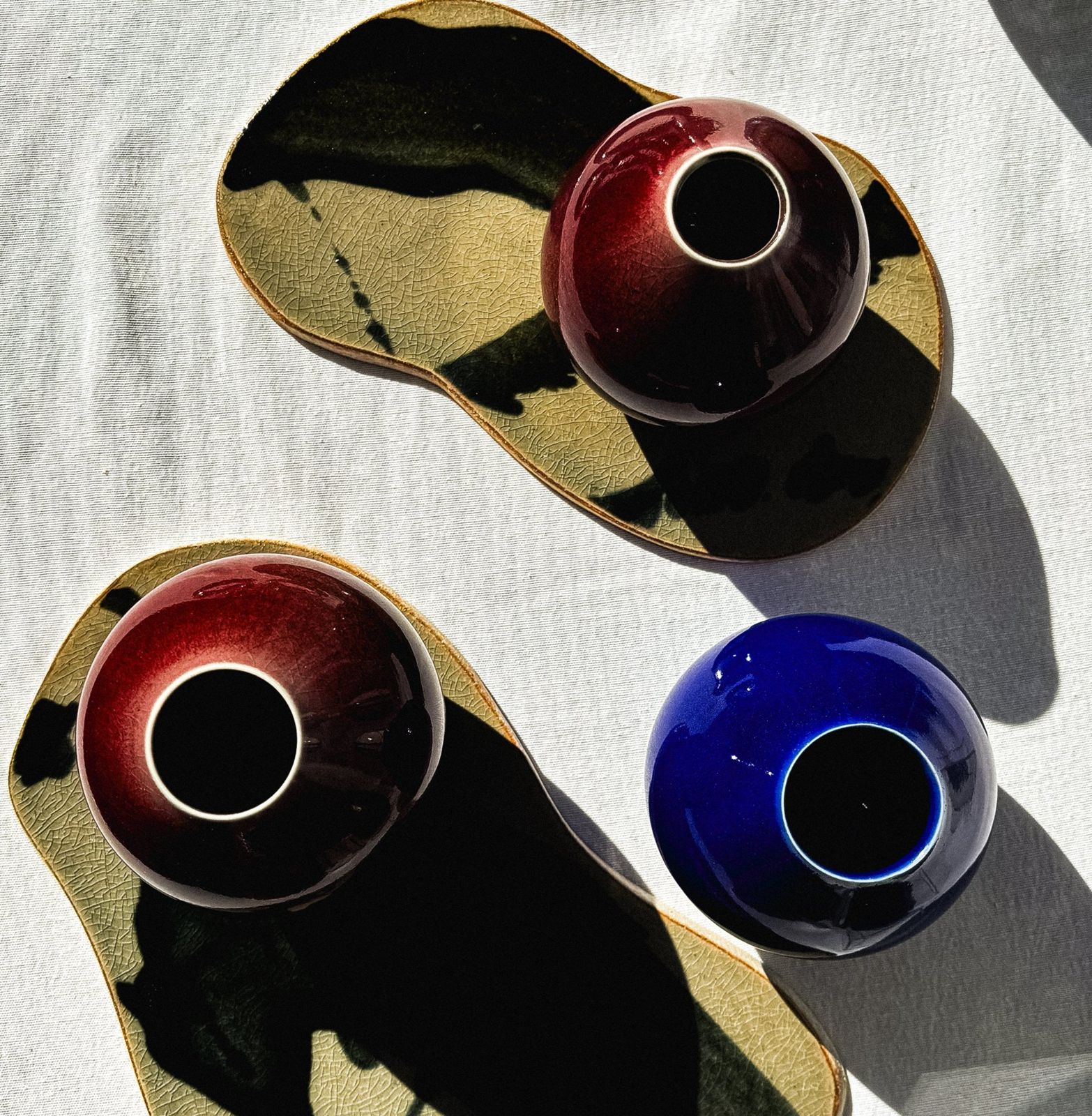 Red and cobalt bud vases on crackled celadon trays in sunlight