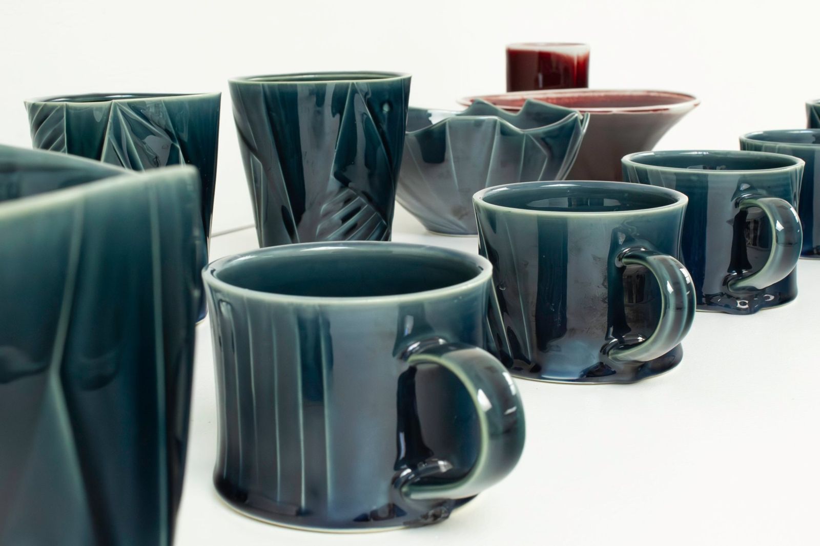 Row of faceted blue-green porcelain mugs and bowls