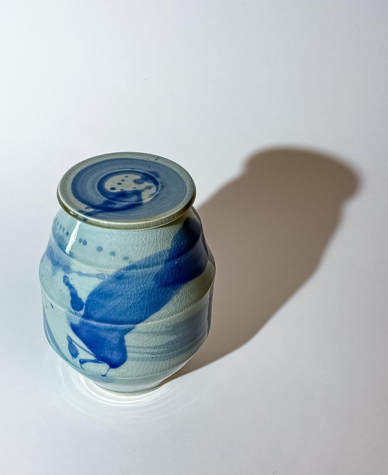 The celadon lidded jar from above, casting a long shadow