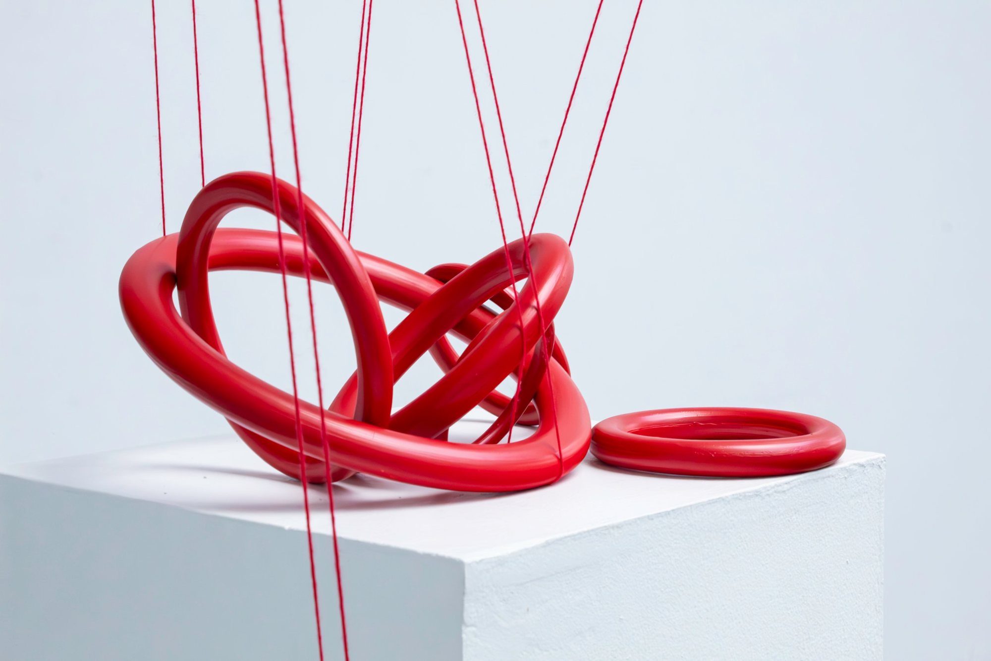 Red porcelain ring knot on a white plinth, held by red threads