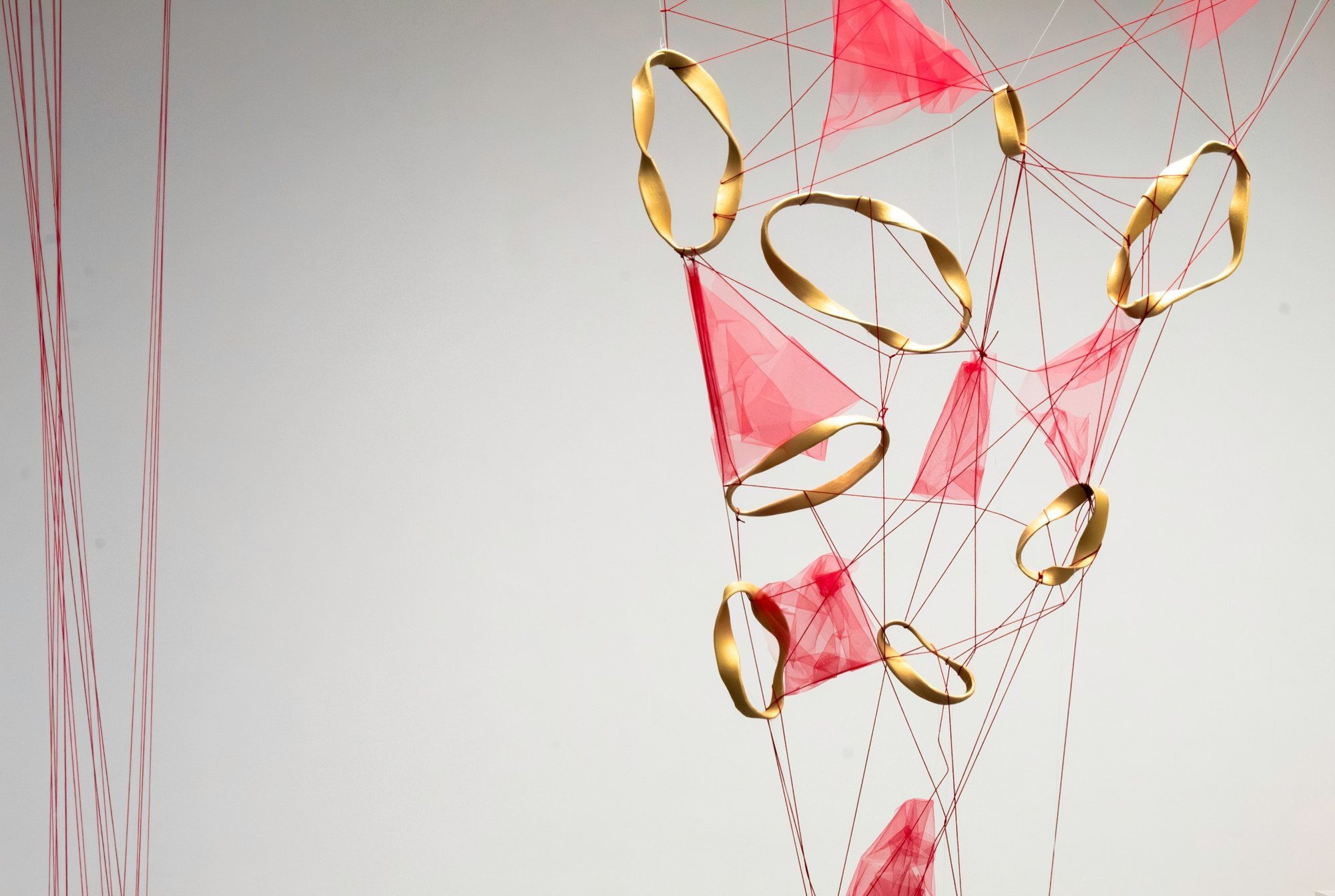 Suspended installation of twisted gold porcelain rings and pink tulle tied with red thread