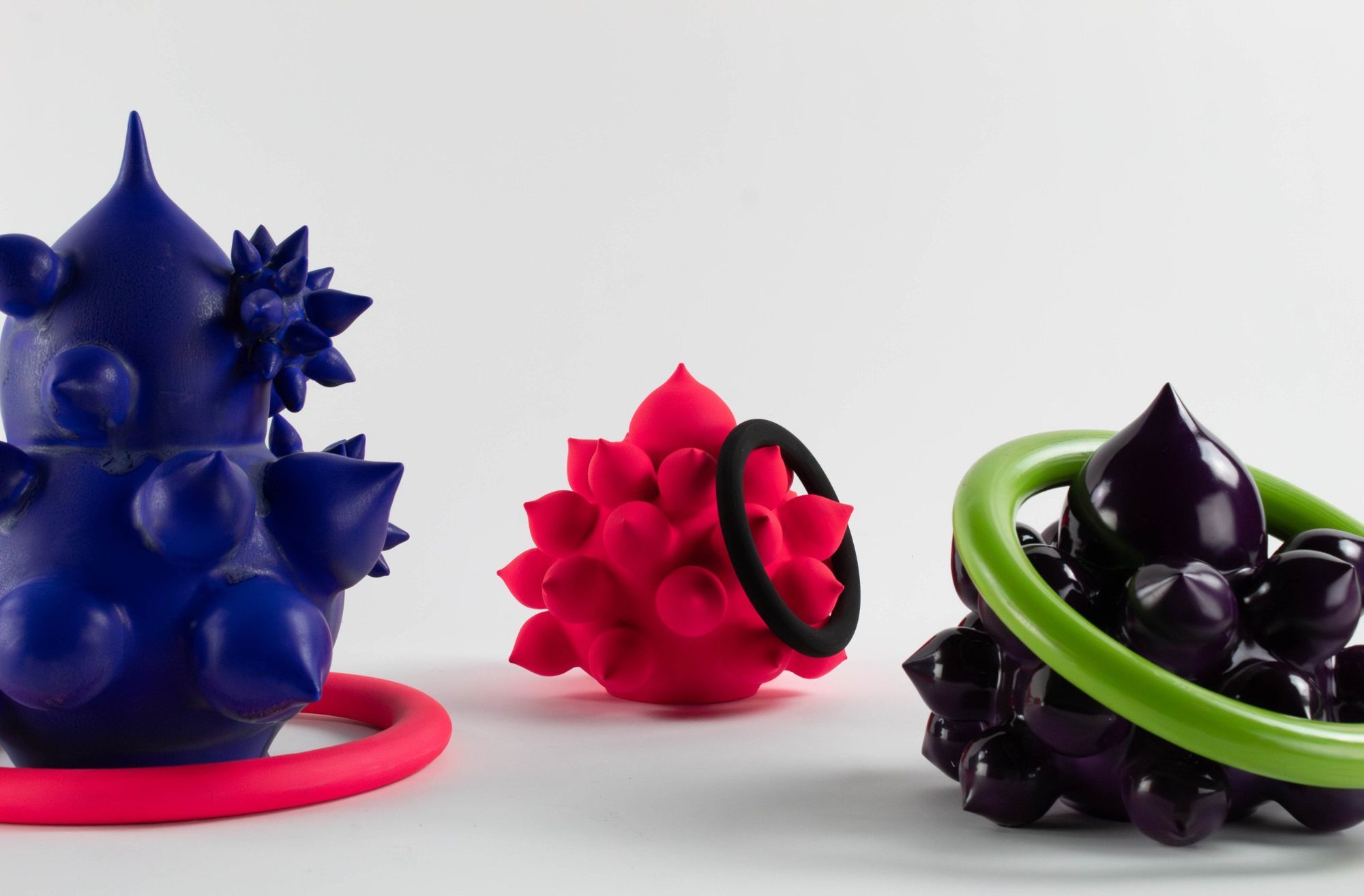 Cobalt spiked form in a pink ring, pink spiked form with a black ring, and an aubergine cluster in a green ring