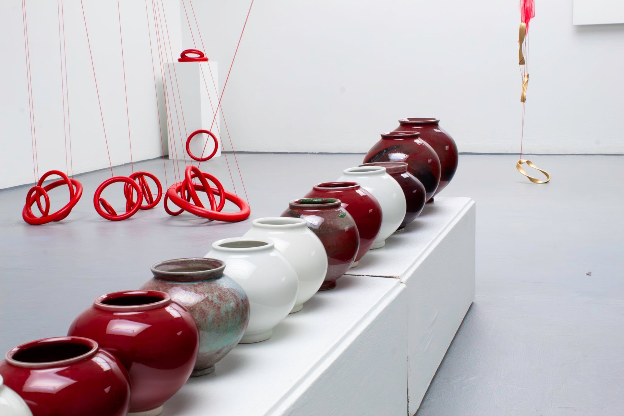 Row of red and white porcelain moon jars on a low plinth