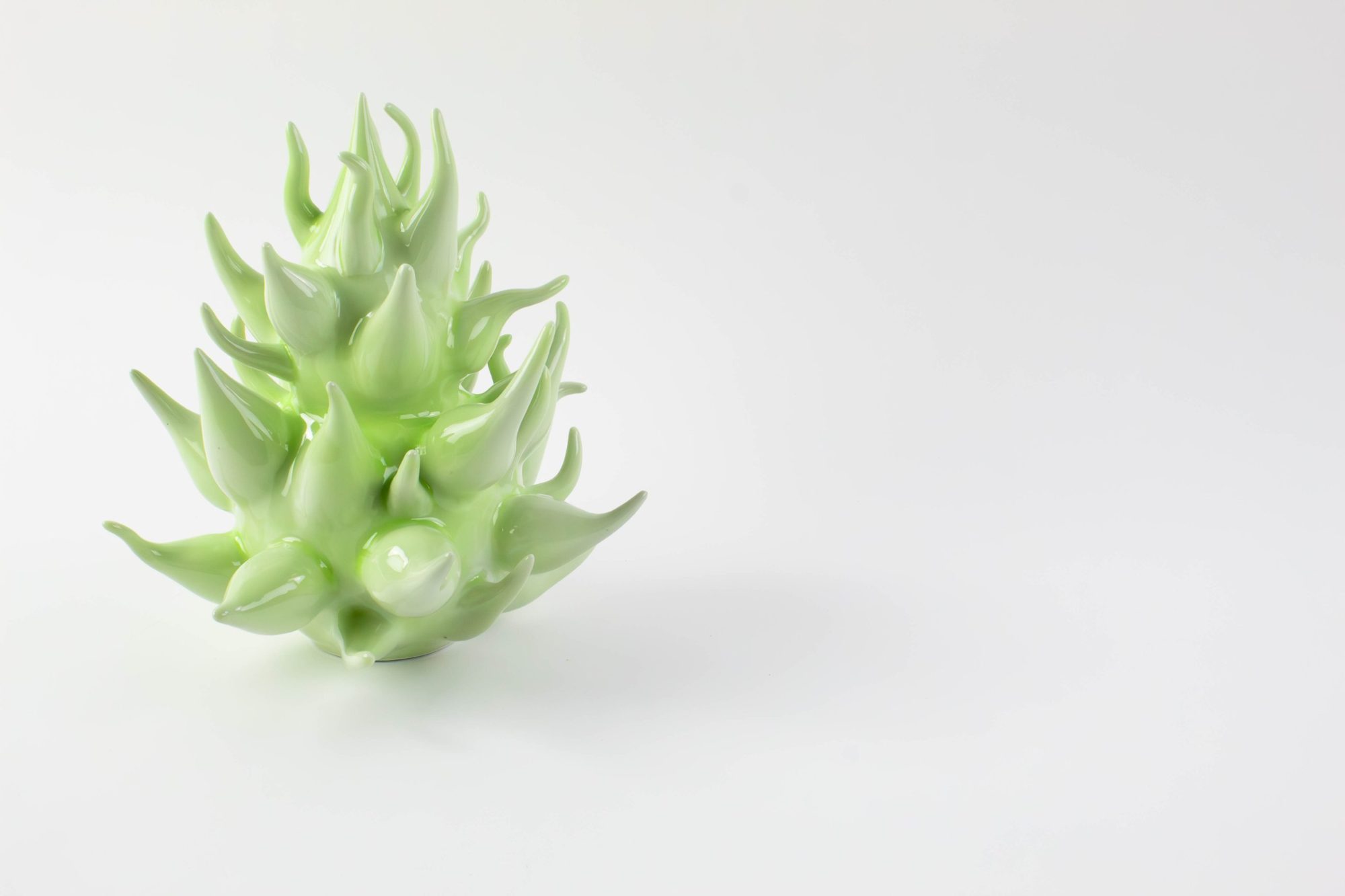 Pale green porcelain form with curling glossy spikes, on white