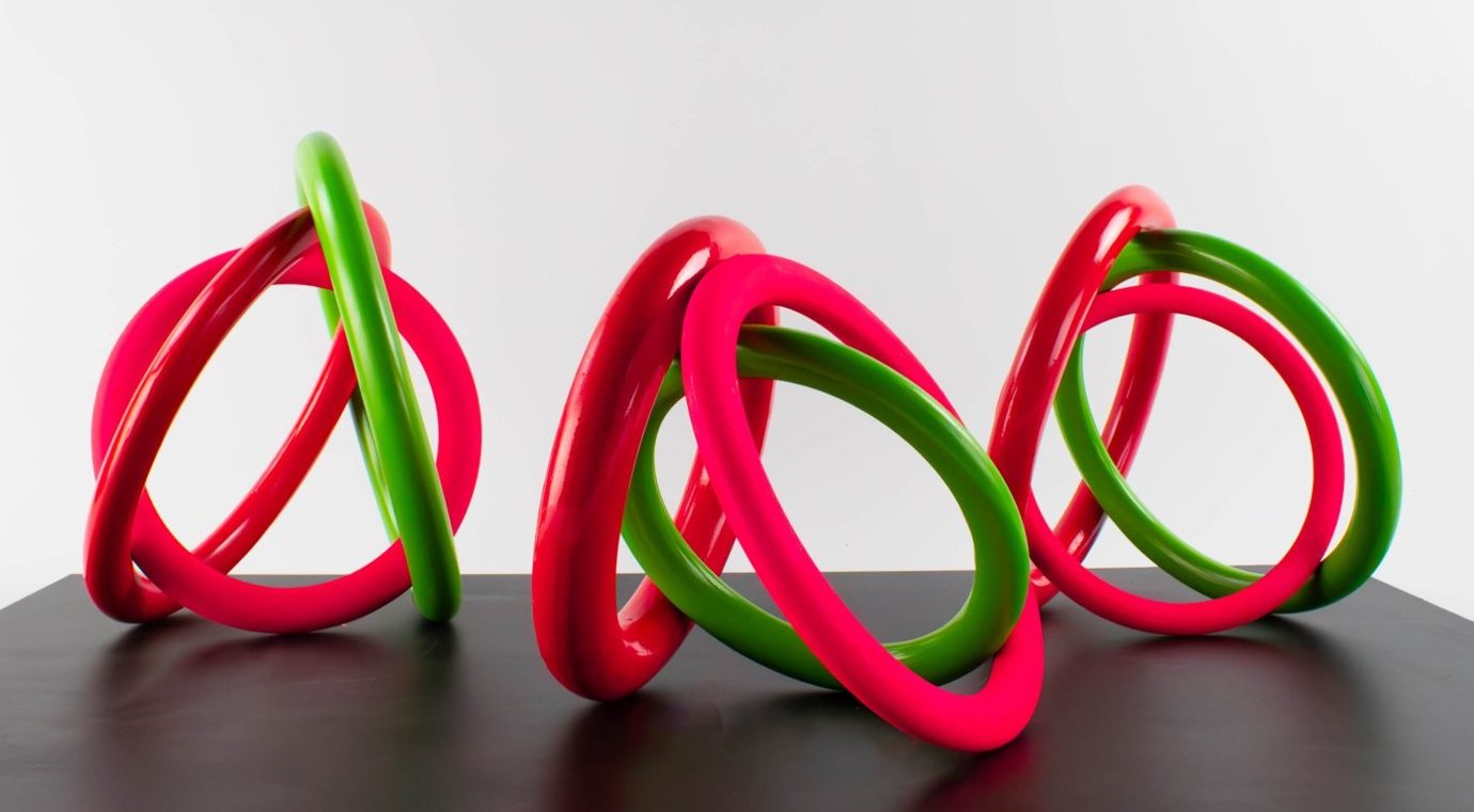 Three knots of pink and green porcelain rings on a black plinth